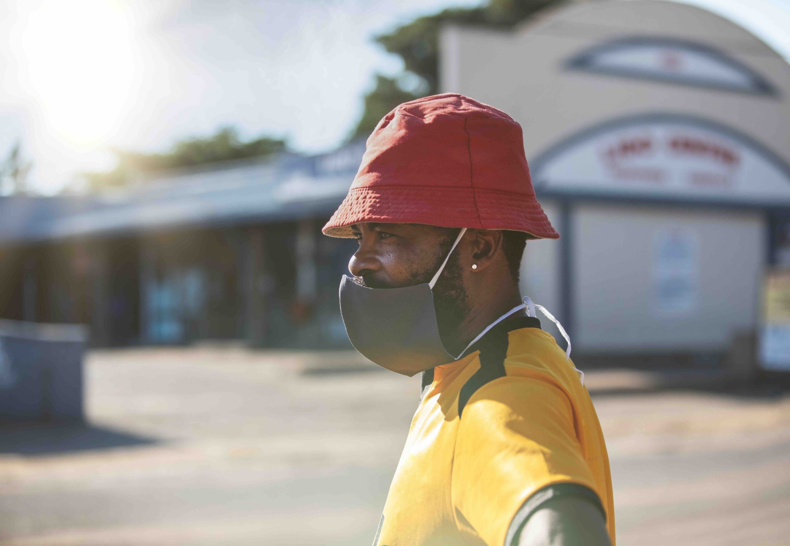 Homme africain dans la rue en Afrique du Sud portant un masque et un chapeau rouge