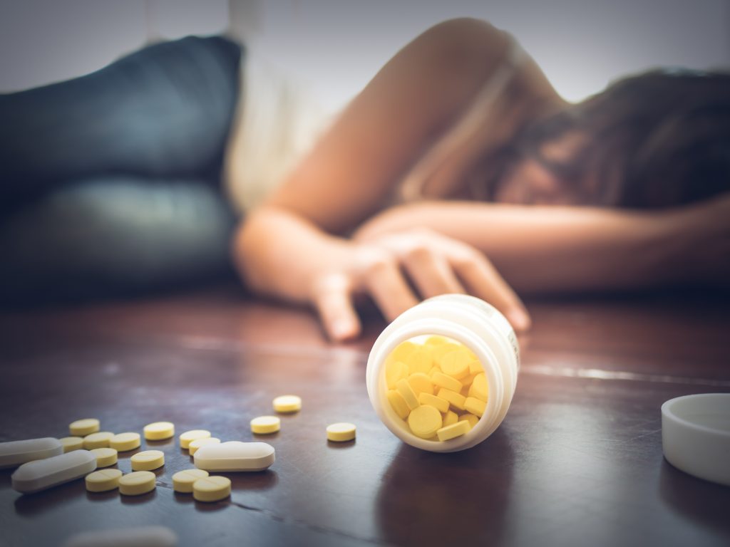 Femme prenant une overdose de médicaments, allongée sur le sol en bois avec une bouteille de pilules ouverte. Overdose ou suicide. @Adobe stock